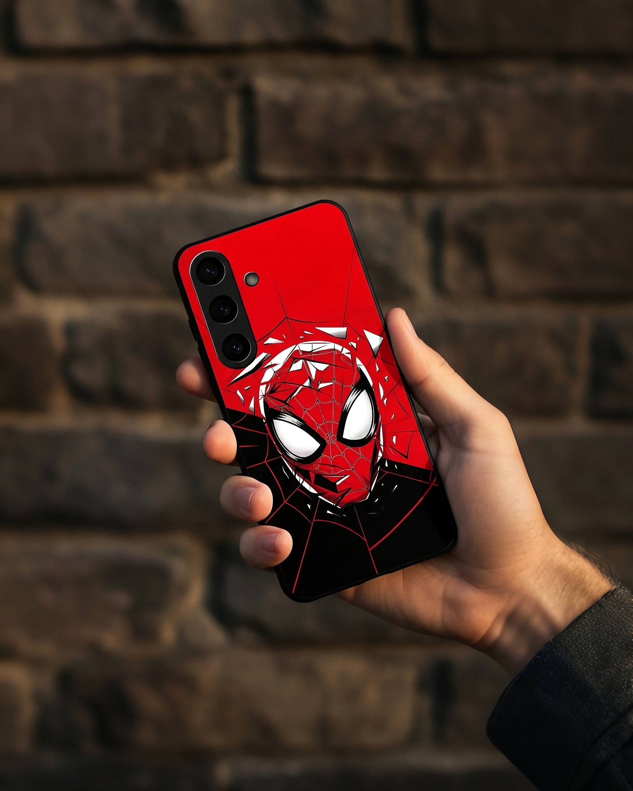 Hand holding a smartphone with a red and black superhero-themed case against a brick wall.