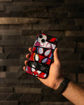 Hand holding a phone with a colorful case against a dark stone wall.